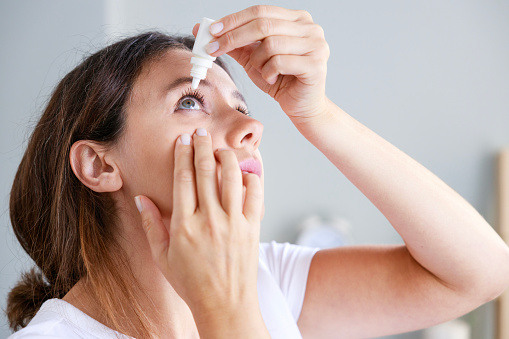 Young woman putting eye drops at home